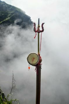 a tall pole with a clock on it in the middle of some foggy mountains