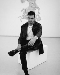 a man sitting on top of a white cube in front of a wall with a statue behind him