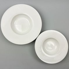 two white plates sitting next to each other on a gray tableclothed surface with one empty plate in the middle