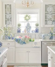 a white kitchen with blue and white dishes on the counter top, vases filled with flowers