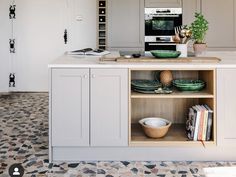 a kitchen with white cabinets and an island in the middle is filled with plates, bowls and books