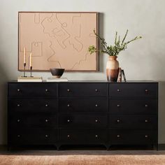 a black dresser with two vases and a painting on the wall