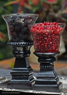 two glass vases filled with berries sitting on top of a metal tray next to each other