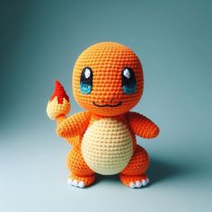 an orange crocheted stuffed animal sitting on top of a gray surface with blue eyes