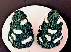 two green christmas trees are sitting on a white plate, one is made out of plastic