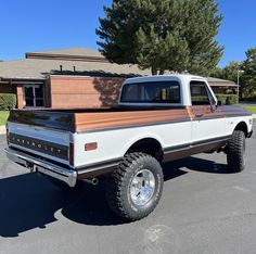 a white pickup truck parked in a parking lot next to a tree and building with brown trim