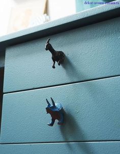 two small toy animals on top of a blue dresser with metal handles and knobs