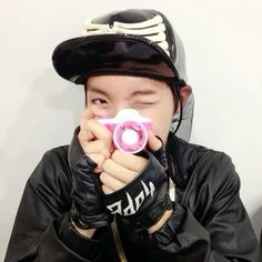 a young boy wearing a black leather jacket holding a pink camera to his face with both hands