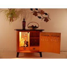 a wooden cabinet with wine glasses and bottles in it next to a potted plant