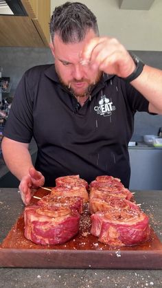 a man in black shirt cutting up some meat on wooden board with utensils