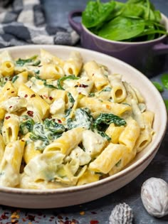 a bowl filled with pasta and spinach on top of a table next to shells