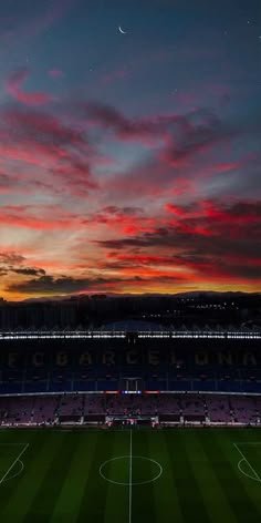 a soccer field at night with the sky lit up and clouds in the background as the sun sets