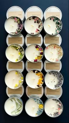 twelve tealight candles in tins with floral designs and labels on the lids, all lined up against a black background