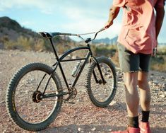 a person standing next to a bike on a dirt road