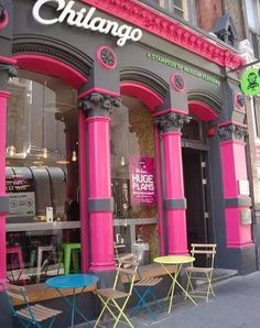 the front of a restaurant that has pink columns and chairs in front of it,