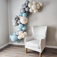 a white chair sitting in front of a wall with balloons hanging from it's sides