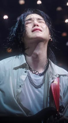 a man with long hair wearing a white shirt and silver necklace is looking up at the sky