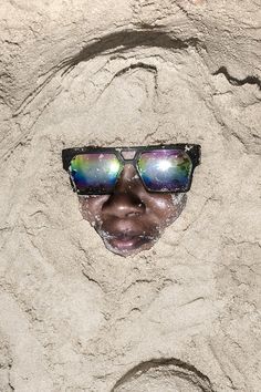 a woman wearing sunglasses in the sand with her face partially hidden by it's reflection