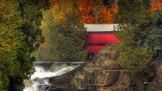 a red covered building sitting on top of a cliff next to a forest filled with trees