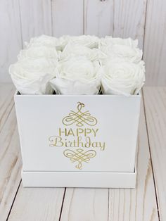 a white box filled with roses on top of a wooden table and the words happy birthday written in gold foil