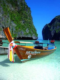 two boats on the beach with cliffs in the background and clear water around them,