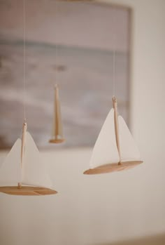 three wooden sailboats suspended from strings in a room with a painting on the wall