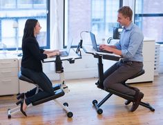 a man and woman sitting at desks with laptops on their laps, using the same chair