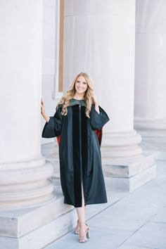 a woman wearing a graduation gown and holding her hand up in the air while standing next to columns