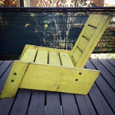 an old yellow wooden chair sitting on top of a wooden deck next to a fence