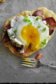 three small pastries with an egg on top and bacon in the middle next to a fork