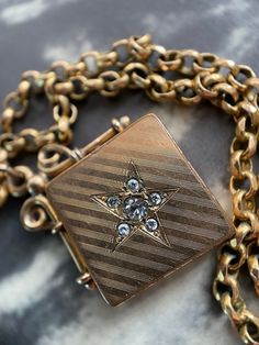 "A crisp and sharp late Victorian square, diagonally set locket. It is gold filled, testing at 14k, and features a central paste starburst set into wonderful geometric pin stripping to the front. The bale and mounting are ornate and well wrought.  The square shape, as well as the style of bale, both indicate that this piece was originally worn on a watch chain as a fob. It opens easily with the help of a small notch on one side, and clicks shut securely. Once open, the plain interior reveals the paste stones to be set open backed; punched through the metal of the locket's front half. The inter of its back half other side reads \"W & H Co\" inside of a heart indicating its manufacturer:a Wightman & Hough, jewelers from Providence, Rhode Island. Active between 1856-1922, they became well reg Antique Engraved Square Pendant Jewelry, Vintage Gold Star Jewelry, Antique Square Locket Pendant Jewelry, Vintage Square Pendant Jewelry Engraved, Antique Square Pendant Locket Jewelry, Vintage Engraved Square Pendant Jewelry, Vintage Square Pendant Locket Jewelry, Vintage Square Pendant Locket, Vintage Square Pendant Jewelry For Anniversary