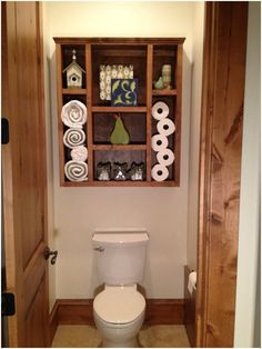 a white toilet sitting inside of a bathroom next to a wooden shelf filled with towels