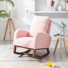 a pink rocking chair sitting on top of a hard wood floor next to a potted plant