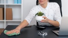 a woman sitting at a desk holding a potted plant in front of her laptop