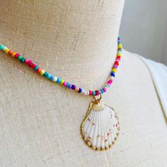 Embrace the essence of summer with this exuberant, colorful beaded necklace, featuring a stunning natural seashell pendant encased in a delicate golden trim. Each bead is meticulously selected to create a kaleidoscope of joy around your neck, reminiscent of a sun-kissed day at the beach or a vibrant festival dance. The heart of this necklace is the seashell pendant, a treasure from the ocean's depths, polished to perfection, and framed in gold. This piece is a celebration of nature's artistry, w Beaded Shell Necklace For Summer Festivals, Summer Festival Beaded Shell Necklace, Summer Beach Beaded Shell Necklace, Colorful Beads Shell Necklace For Summer Vacation, Beachy Strand Necklace With Colorful Beads, Summer Vacation Shell Necklace With Colorful Beads, Beach Shell Necklace With Beaded Chain, Beaded Shell Strand Necklace For Beach, Beaded Shell Necklace For Beach Vacation