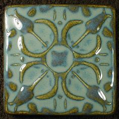 a blue and green square tile with birds on it's sides, sitting on the floor