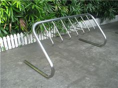 a metal bike rack sitting in front of a white picket fence with green plants behind it