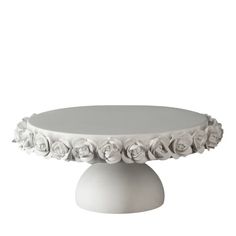 a white cake stand with flowers on it's sides and a round base in the middle