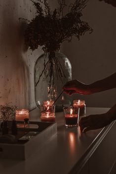 a person lighting candles on a counter in front of a vase filled with flowers and branches