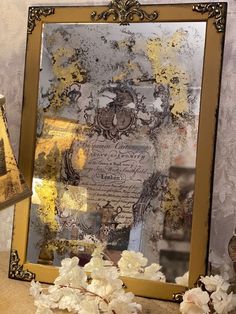 an ornate gold framed mirror sitting on top of a table next to flowers and a lamp