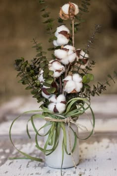 a white vase filled with cotton and greenery