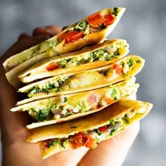 a person holding a stack of tortilla shells with toppings on them in their hands