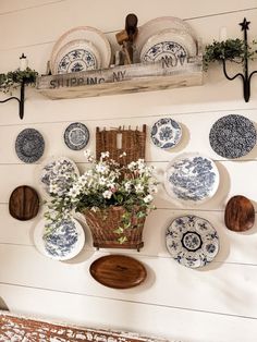 blue and white plates are hanging on the wall above a basket with flowers in it