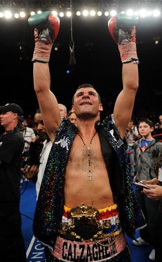 a man with his hands up in the air at a boxing match, surrounded by fans