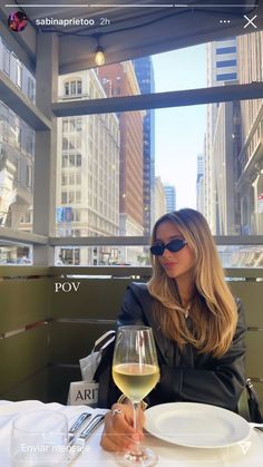 a woman sitting at a table with a glass of white wine in front of her