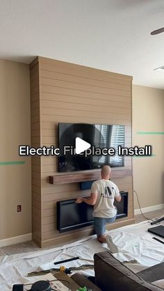 a man standing in front of a flat screen tv on top of a wooden wall