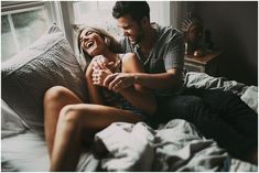 a man and woman sitting on top of a bed next to each other smiling at each other