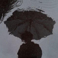 the reflection of a person holding an umbrella is shown in the water as it reflects on the ground