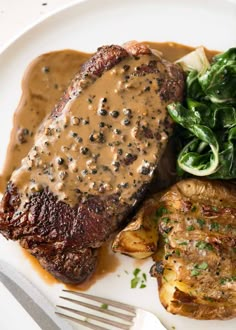 a white plate topped with meat and potatoes covered in gravy next to greens