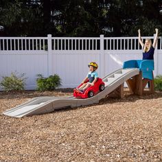 two women and a child are playing on a slide in the yard with their hands up